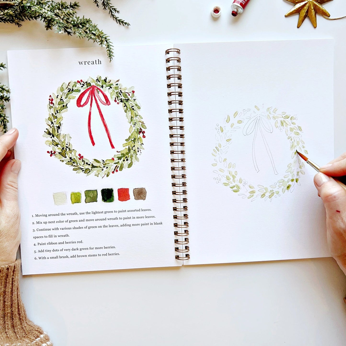 Open book with a wreath illustration and color guide on a white surface.