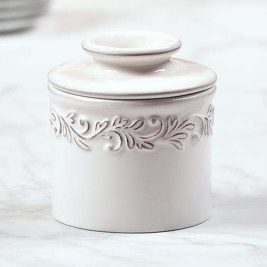 The Antique White linen Butter Bell Crock it has a design around the top of the base that is highlighted with a bronze glaze relief.