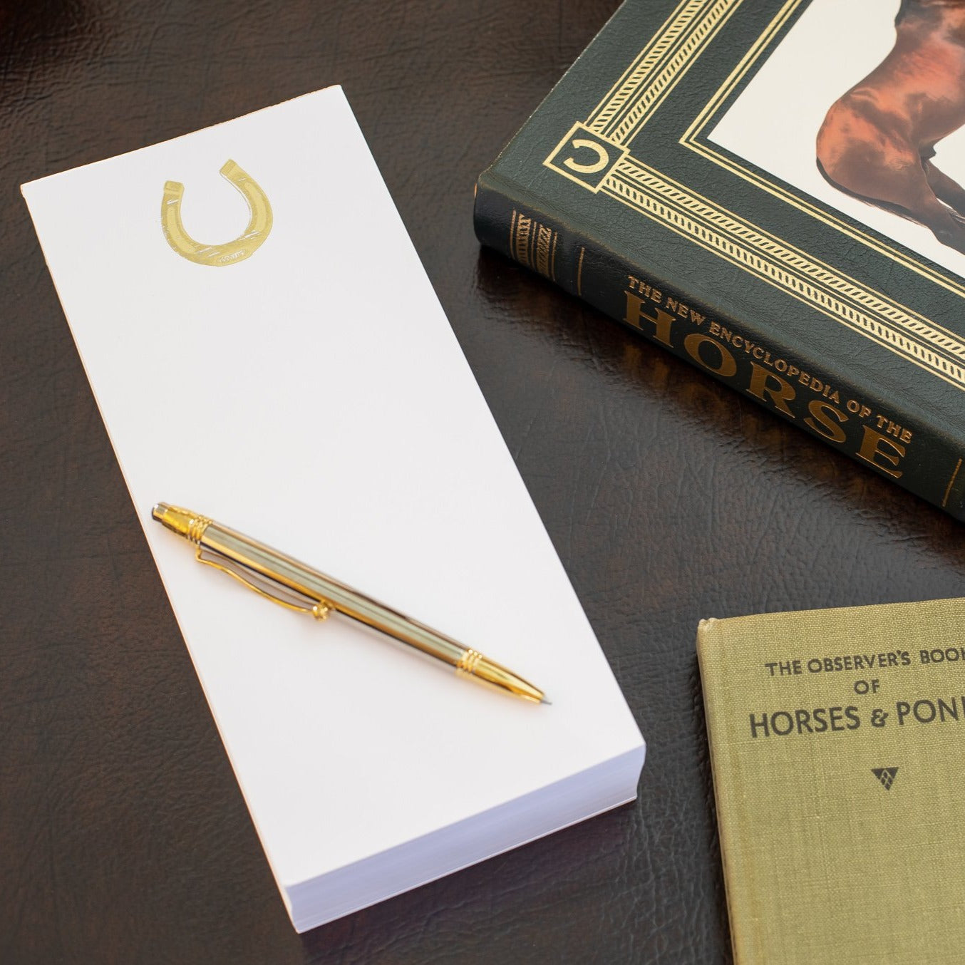 A photo of the Gold Embossed Horseshoe Buck note pad setting with horse books on a desk.