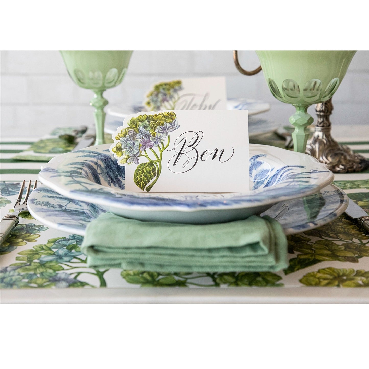 a close up of a table setting using the blooming hydrangeas placemat and place card on a table runnerr