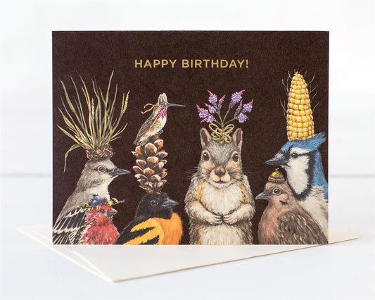 A group of woodland creatures' heads adorned with nature's bounty of flowers, nuts, pinecones, dressed up to wish you Happy Birthday
