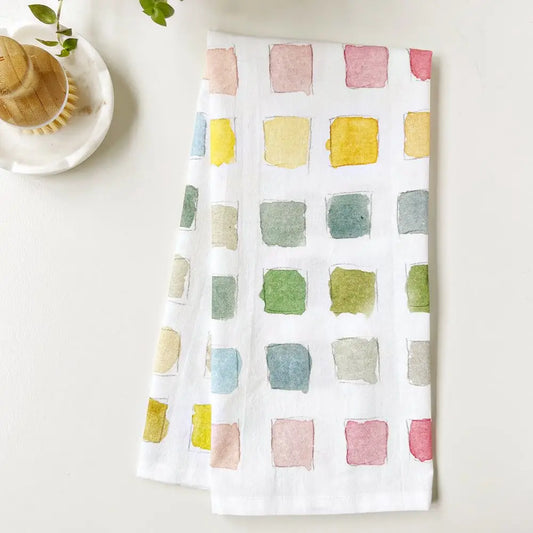 Emily Lex Paint Swatch Tea Towel with watercolor paint swatches in soft pastel tones folded.
