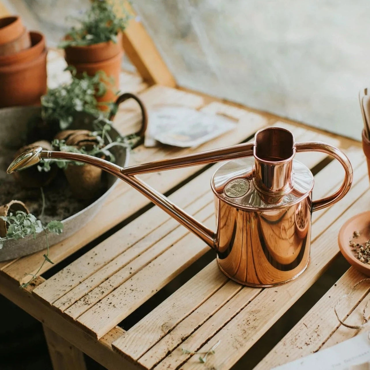 Haws Rowley Ripple Watering Can - 2 Pint Copper setting on a garden workbench