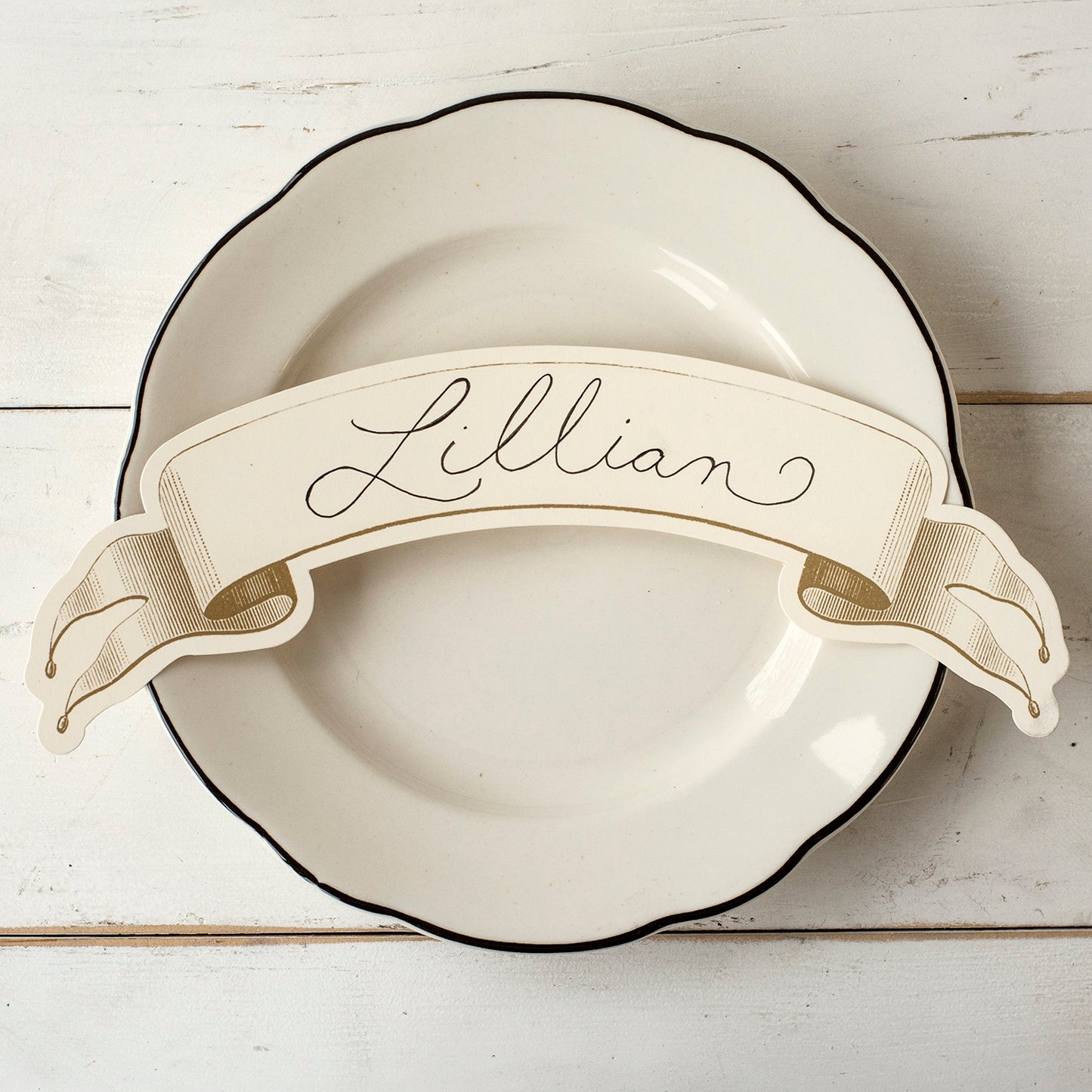 One of the gold banners being displayed as place card on a white and black trimmed plate