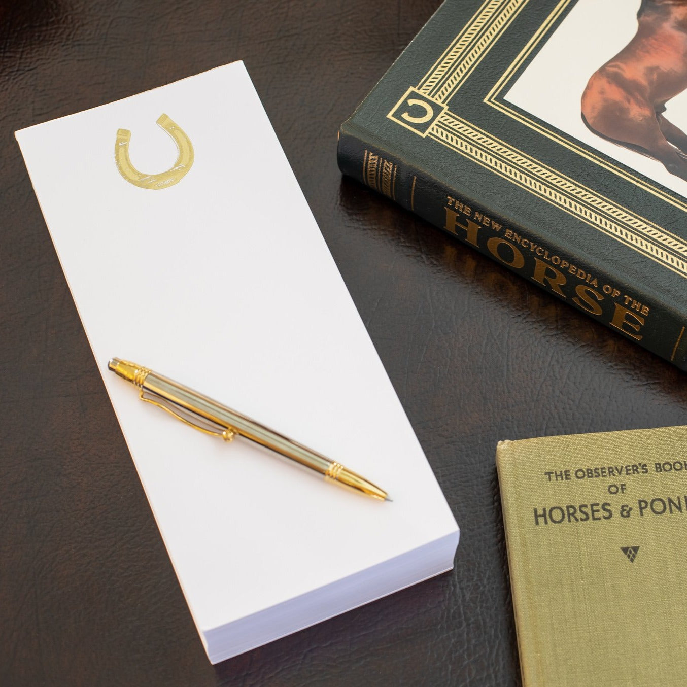 A photo of the Gold Embossed Horseshoe Buck note pad  setting with horse books on a desk.