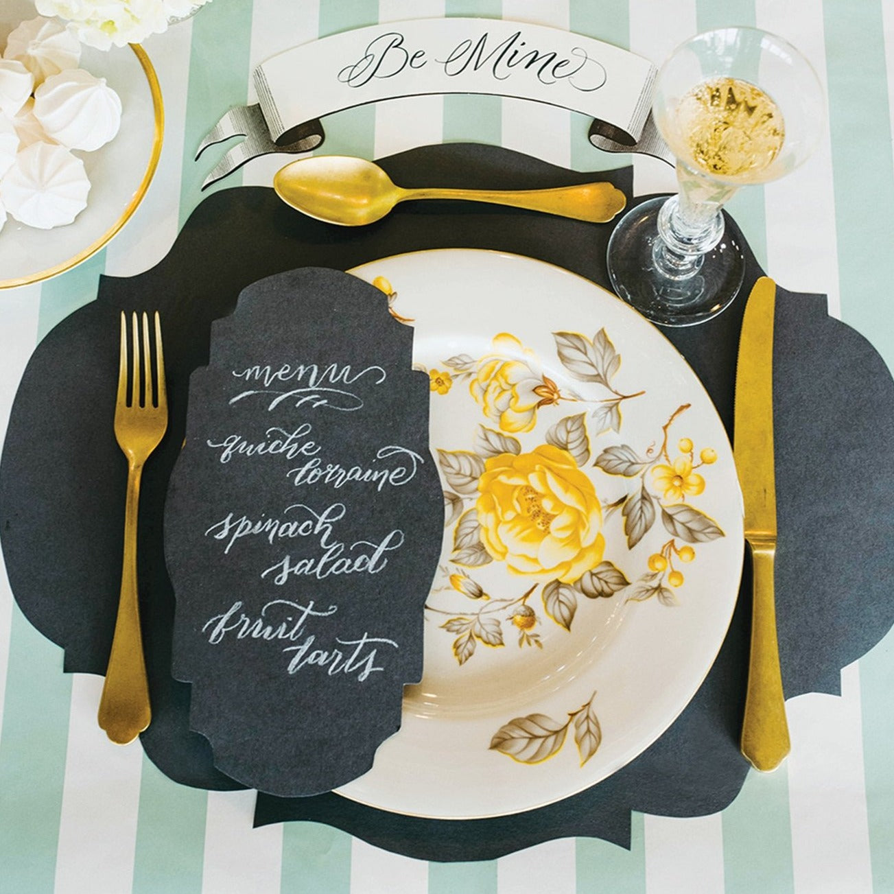 A photograph of the gray french frame placemat in a tablescape. It shows gold silverware and flowered dishes placed on the placemat.