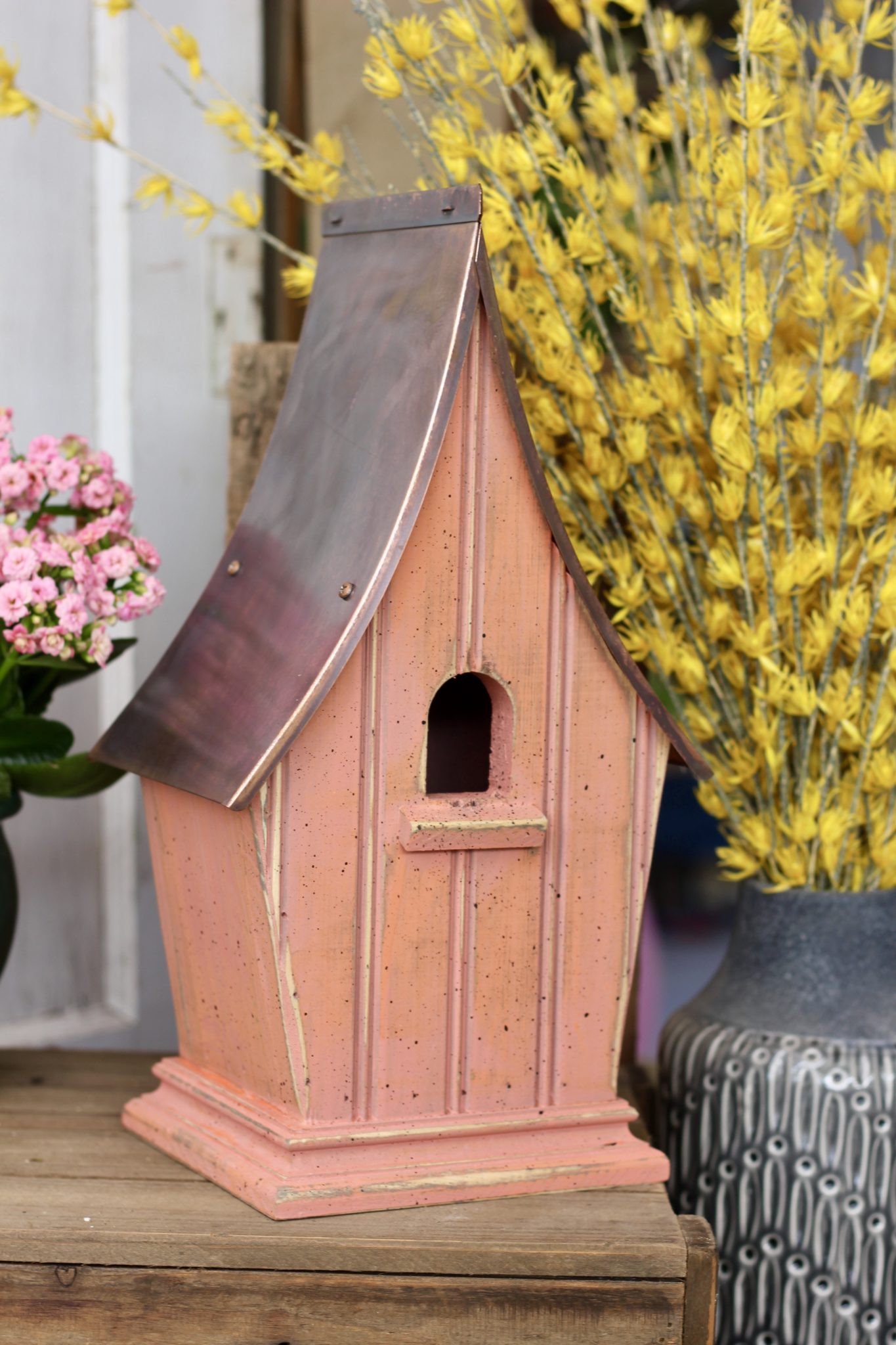 A copper roofed bird house in the color peach.