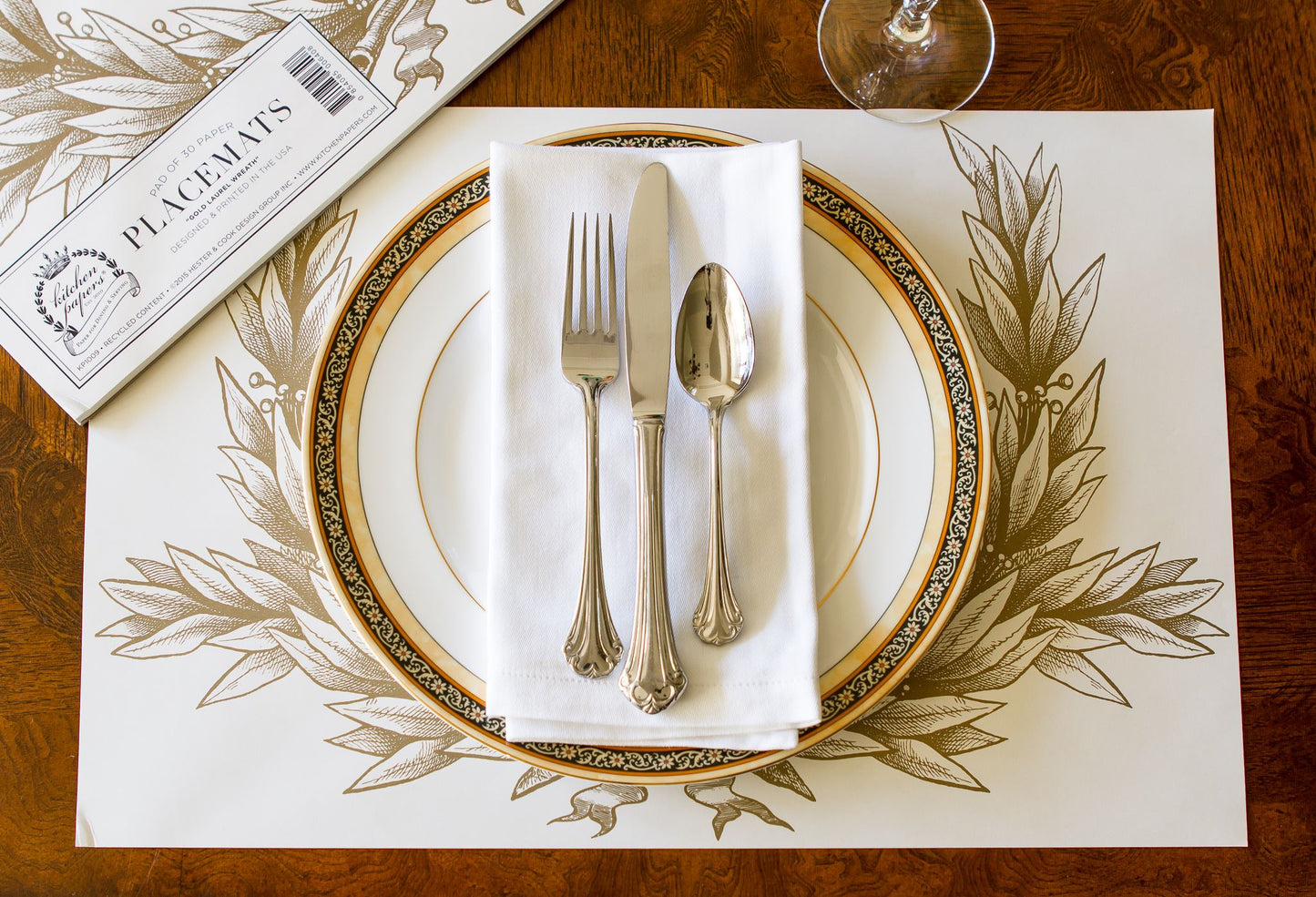 A beautiful place setting using the gold laurel paper placemats with an elegant plate,napkin and silverware.