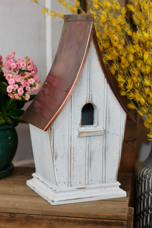 A copper roofed bird house in white.