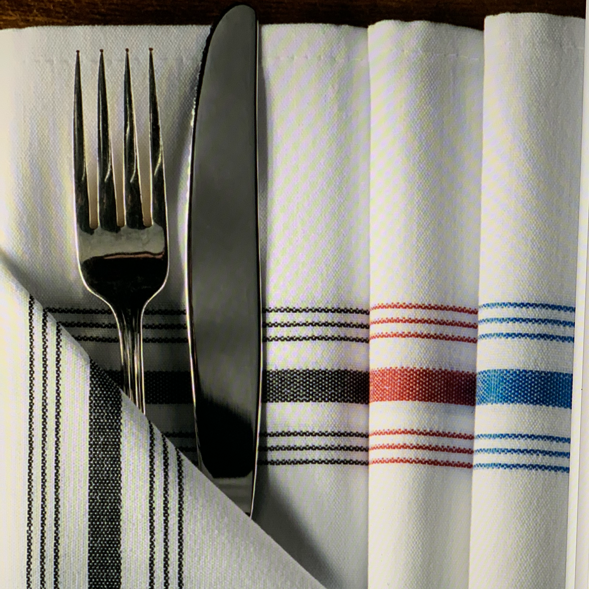 Bistro Striped Napkins in black, red, blue, folded with a fork and knife inserted in the fold.