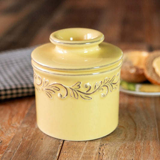 The Goldenrod Butter Bell Crock with intricate embossing that resembles the leaves and crawling vines of a French vineyard, giving the container a well-worn antique appearance. 