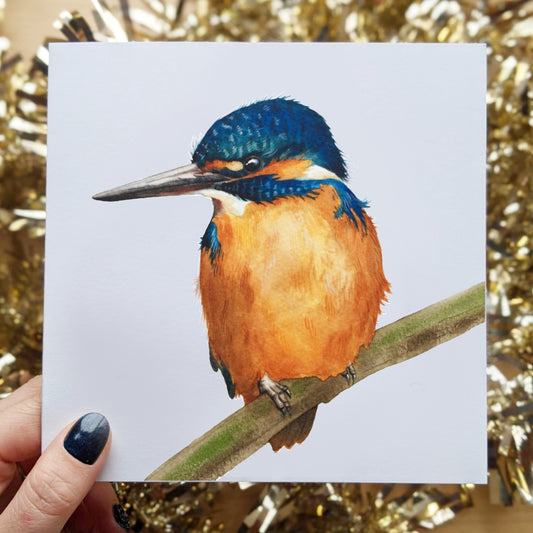 This is a picture of the Kingfisher greeting card. The Kingfisher bird has a bright blue head and a amber color body, sitting on a branch.