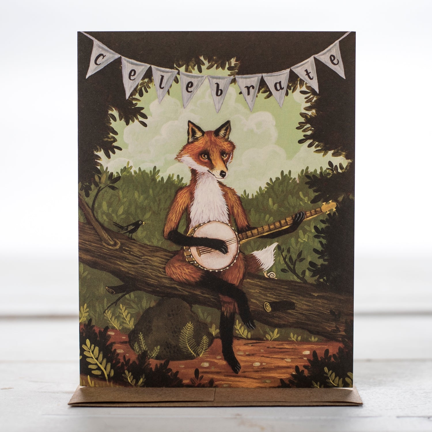 Showing the Fox Celebrate Greeting Gard with a clever Fox sitting on a fallen tree with a banner hanging above his head with the word celebrate spelled out.